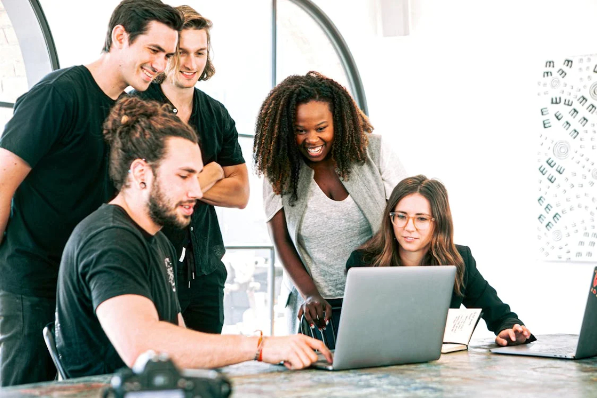A group of individuals collaborates around a laptop at a modern workspace, engaged in discussion.