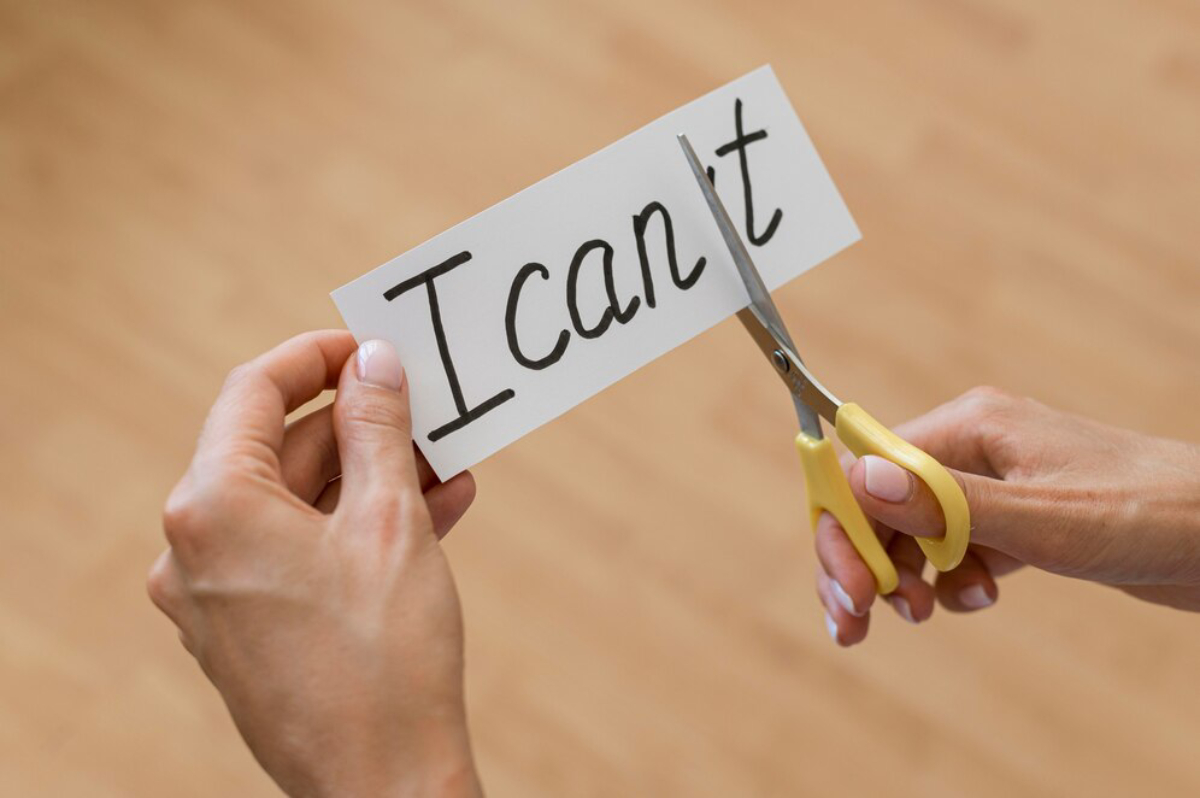 A person with yellow scissors cutting a card that says I can't, symbolizing overcoming limitations.