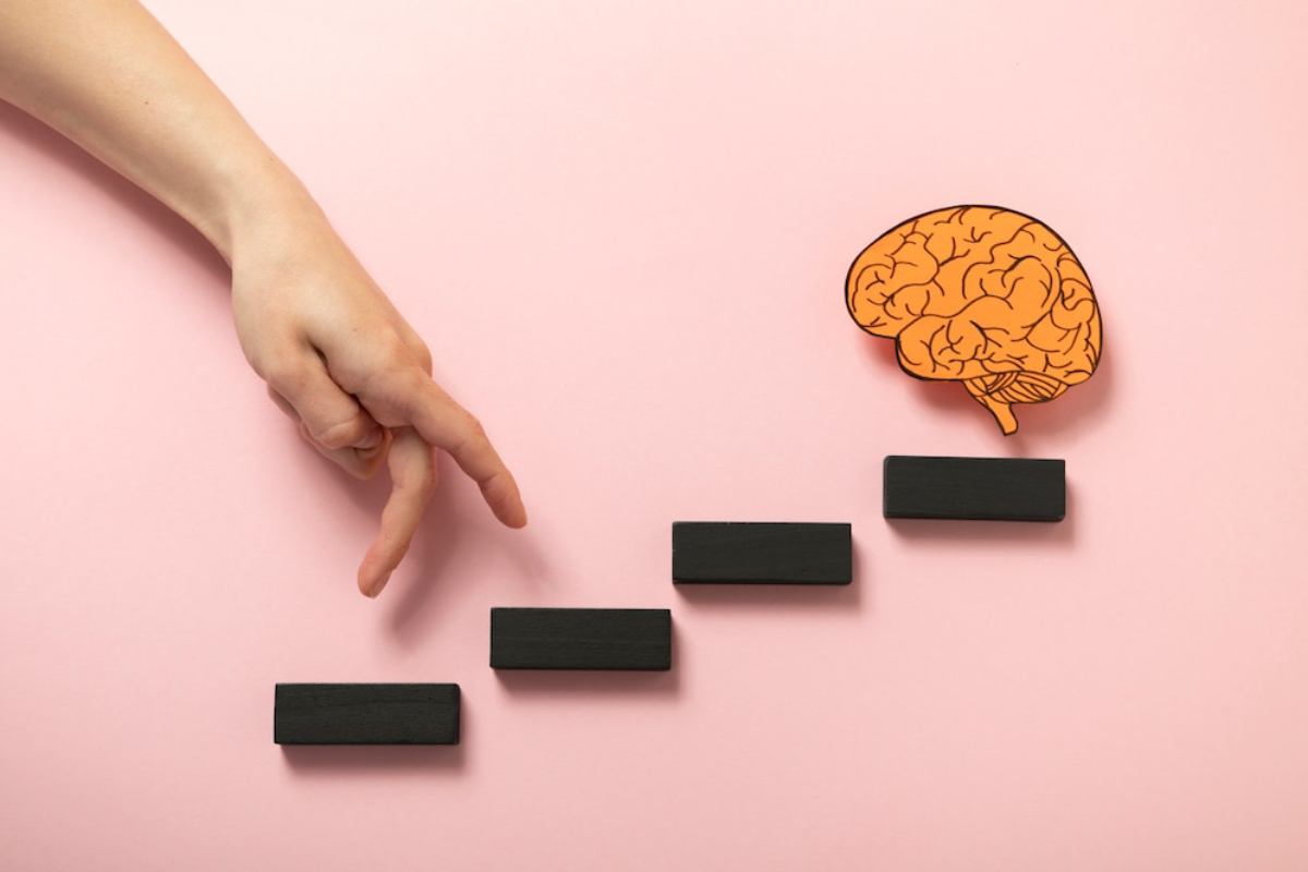 A hand reaches for black blocks arranged like steps, with an orange brain illustration above, symbolizing cognitive development.