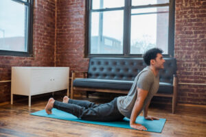 A person practicing yoga in a sunlit room with exposed brick walls, performing the upward-facing dog pose on a blue mat.