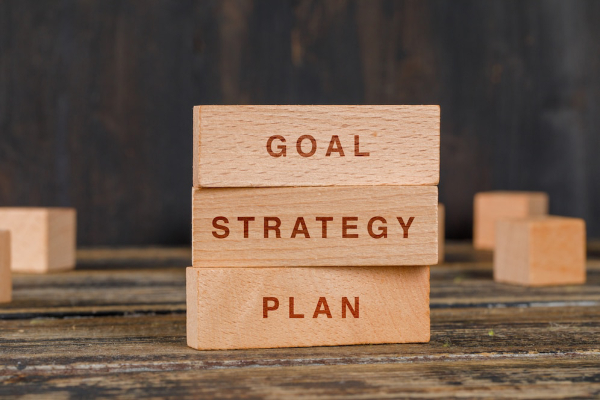 Stacked wooden blocks display the words GOAL, STRATEGY, and PLAN on a rustic wooden surface, emphasizing strategic thinking.
