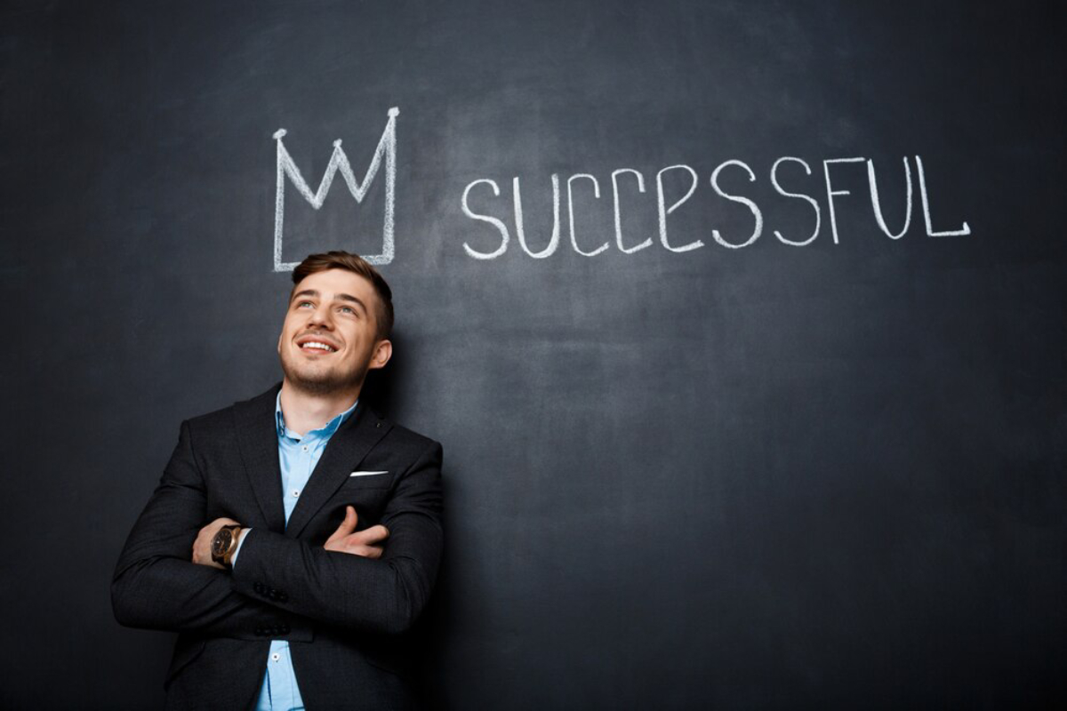 A man in a suit stands confidently against a chalkboard displaying the word SUCCESSFUL and a crown sketch above it.