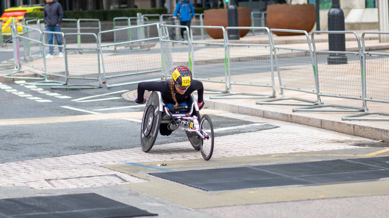 A racer in a wheelchair speeds through a street lined with barriers, showcasing determination and athleticism during a competition.