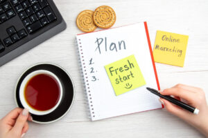 A hand holds a cup of tea beside a notepad listing a Plan.