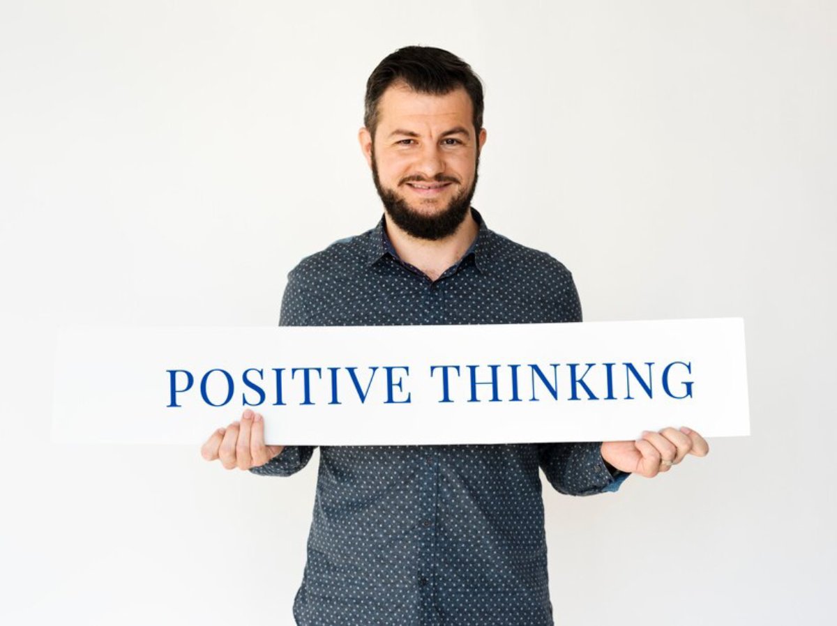 Man smiling holding a sign that reads POSITIVE THINKING.
