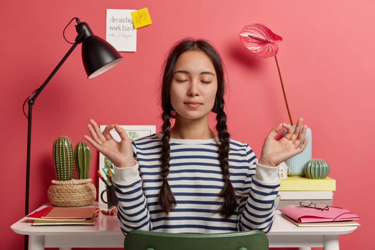 Young woman meditating at a colorful study desk with serene expressions, surrounded by plants and motivational notes.