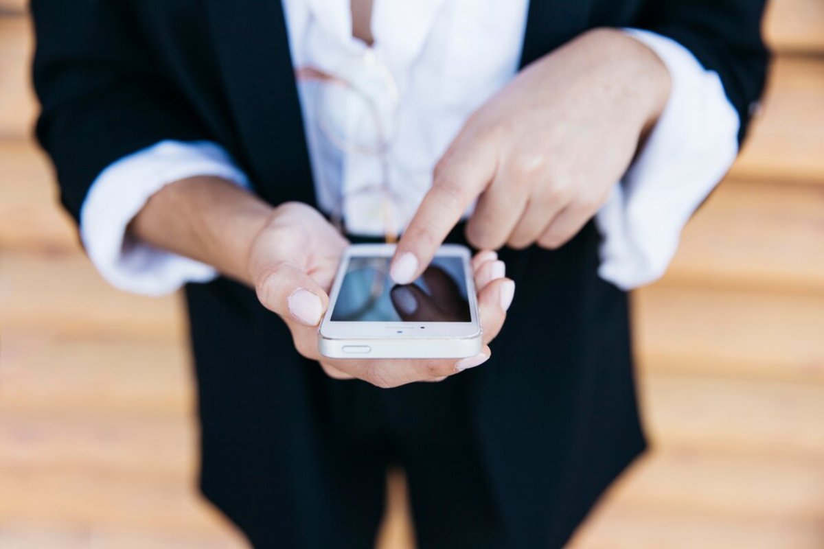 Person in business attire using a smartphone outdoors, focusing on typing a message.
