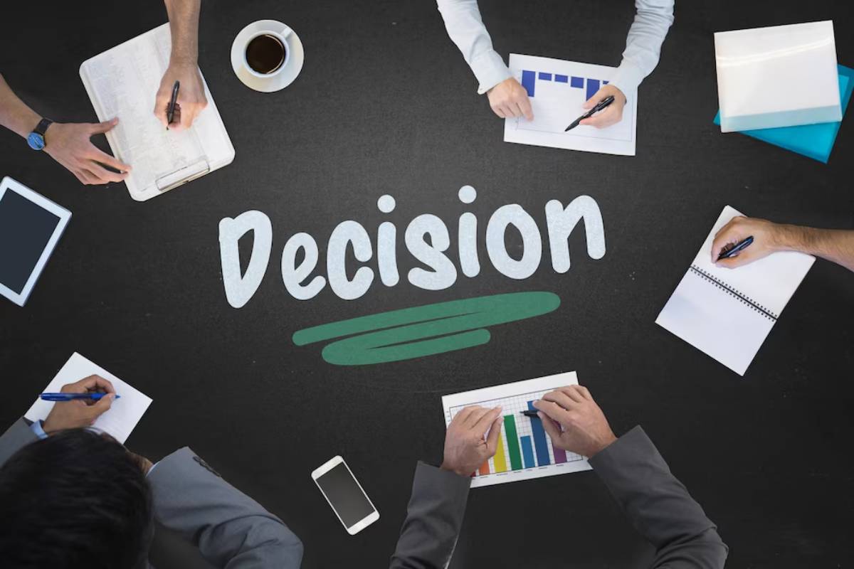 Four professionals working around a table with the word Decision displayed prominently in the center.