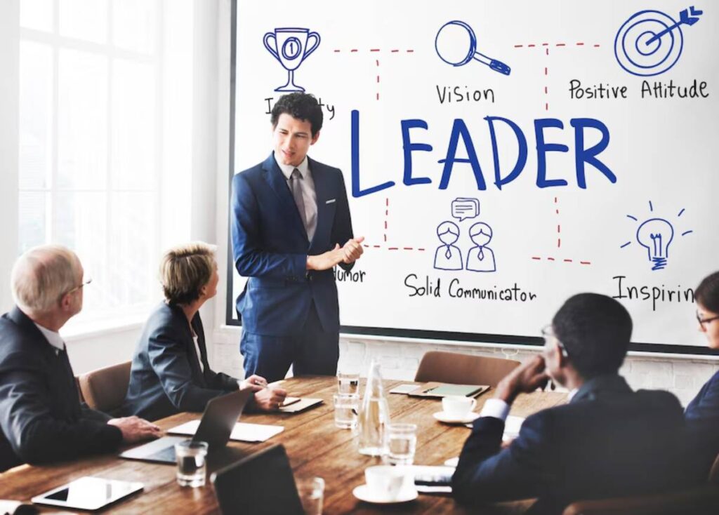 A professional man presents leadership qualities on a whiteboard to attentive colleagues in a conference room.